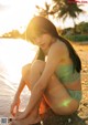 A woman sitting on the beach in a bikini.