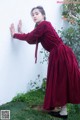 A woman in a red and black dress leaning against a wall.