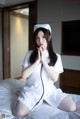 A woman in a white nurse outfit sitting on a bed.