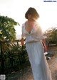 A woman in a white dress walking down a dirt road.