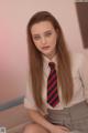 A woman in a school uniform sitting on a bed.