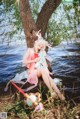 A woman sitting under a tree next to a body of water.