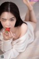 A woman laying on the floor eating a strawberry.