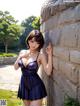 A woman in a blue dress leaning against a stone wall.