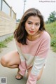 A woman in a pink and white sweater crouching down on the ground.