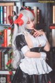 A woman dressed as a maid in front of a bookshelf.