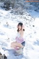 A woman sitting in the snow wearing pink ear muffs.