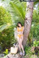 A woman in a yellow bikini leaning against a palm tree.