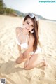 A woman in a white bikini sitting on a beach.