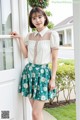 a woman standing in front of a door wearing a white shirt and green skirt