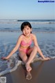 A woman in a pink bikini sitting on the beach.