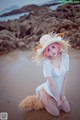 A woman in a white dress and a straw hat on a beach.