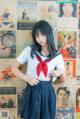 A woman in a sailor outfit posing in front of a wall of posters.